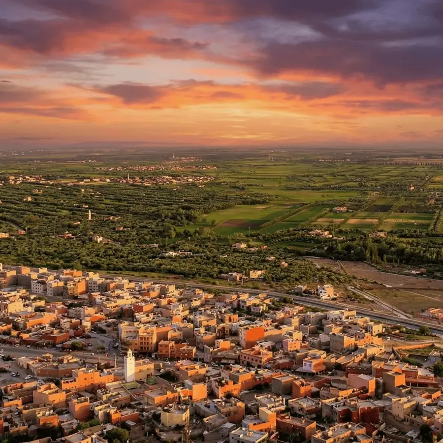 Afourar&rsquo;s ochre rooftops and mosque minaret at sunset, with the irrigated fields of the Tadla plain stretching to the horizon